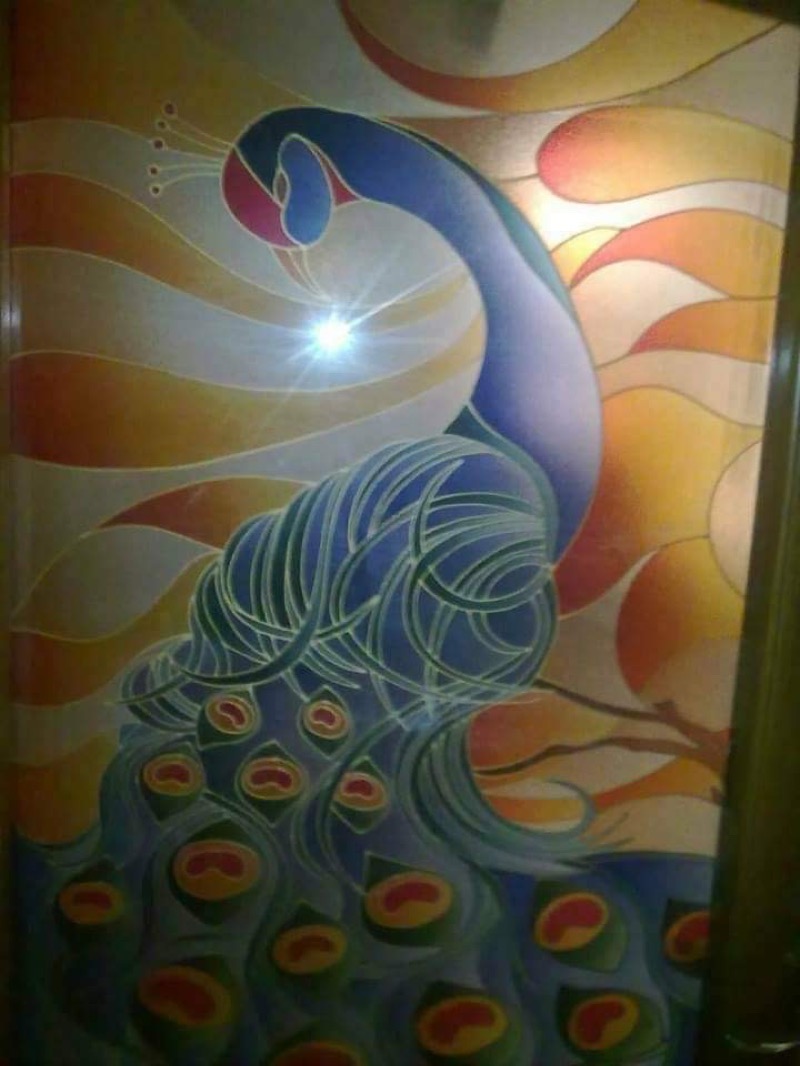 Reverse glass painting of a peacock with flowing blue-teal plumage against a luminous gold background